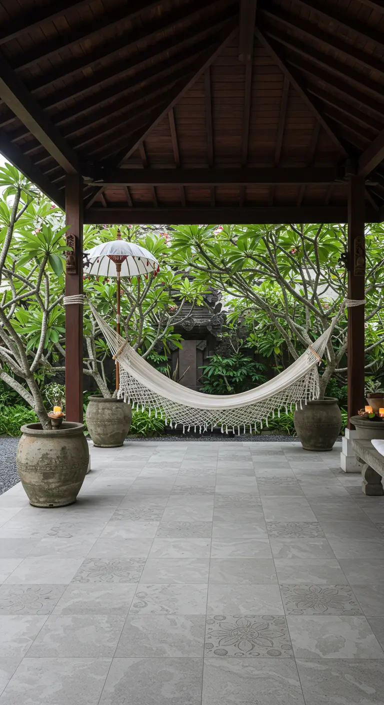 A hammock hangs in a wooden Balinese gazebo surrounded by frangipani trees in stone pots.