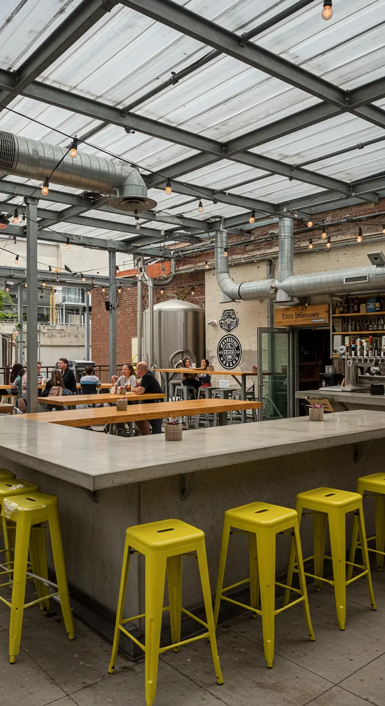Industrial brewery patio with a concrete bar and bright yellow metal stools.