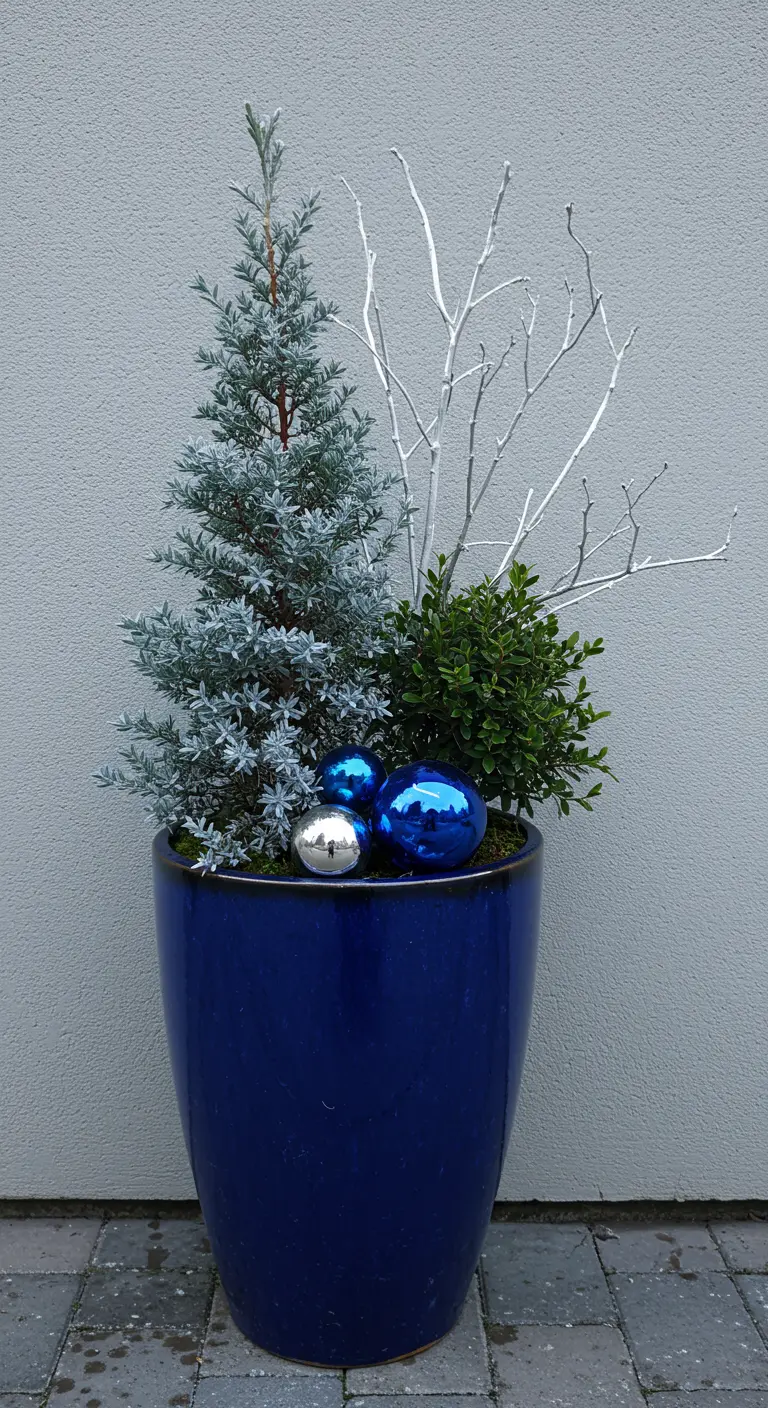 A tall blue planter with a silver-blue juniper, white branches, and blue and silver ornaments.