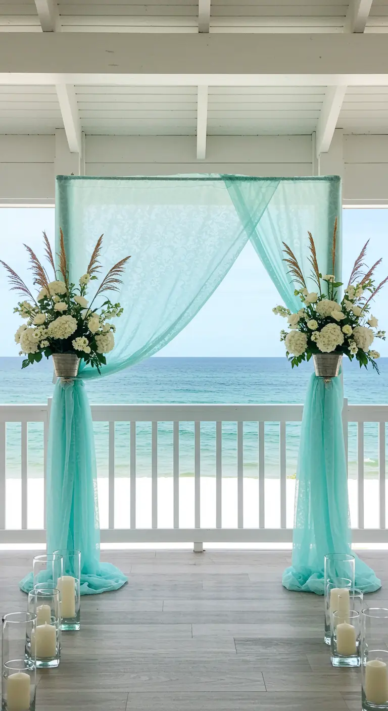 A beachside wedding altar with sheer turquoise fabric and white floral arrangements.