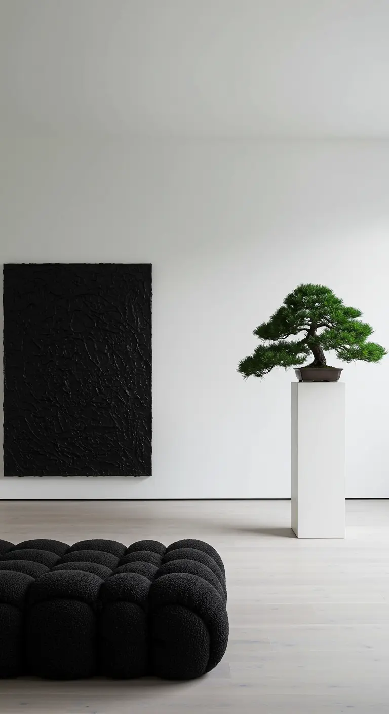 A minimalist white room with a black tufted seat, a black textured painting, and a bonsai on a pedestal.