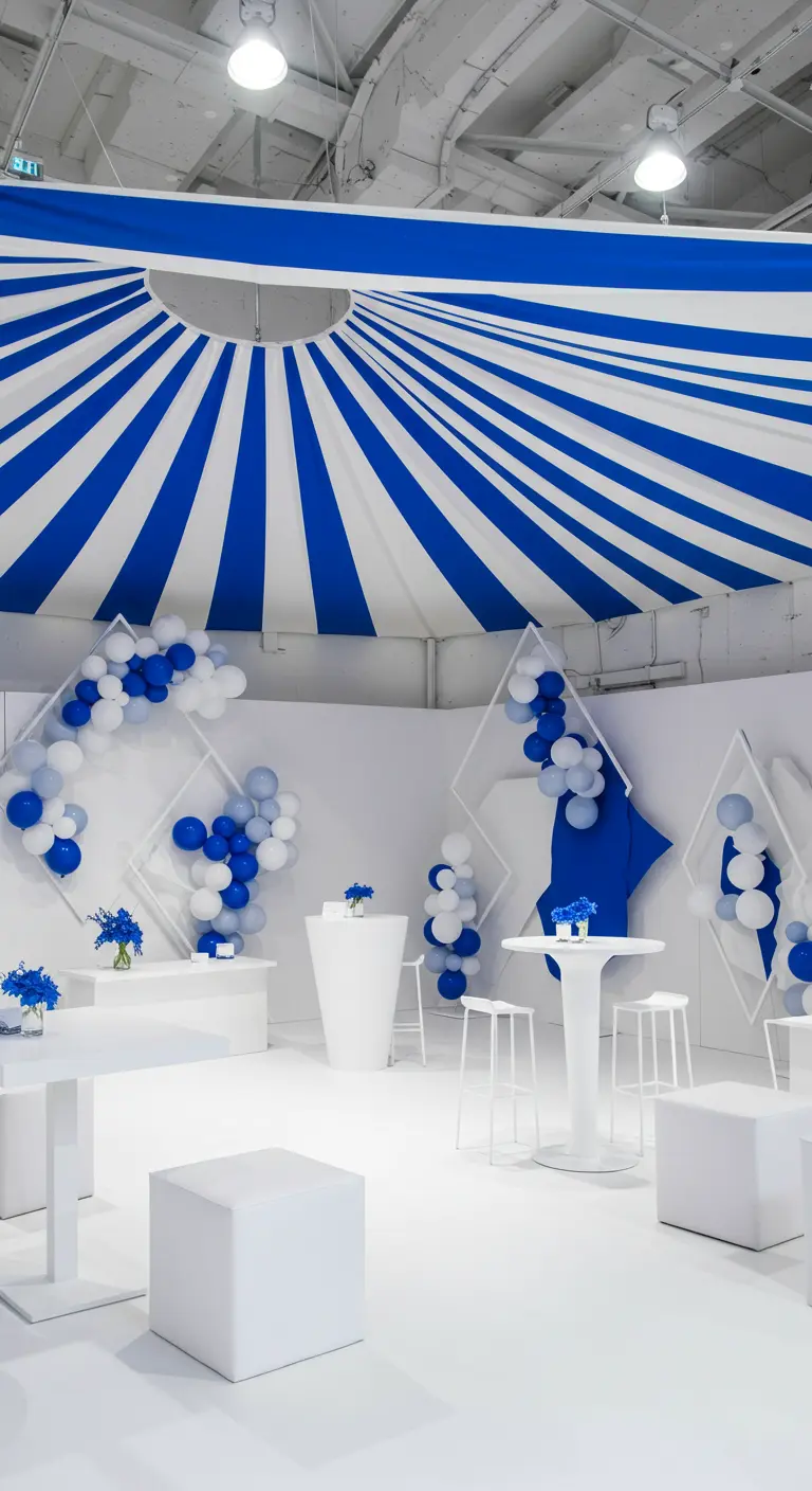A modern party with a blue and white striped canopy, white furniture, and blue balloon accents.