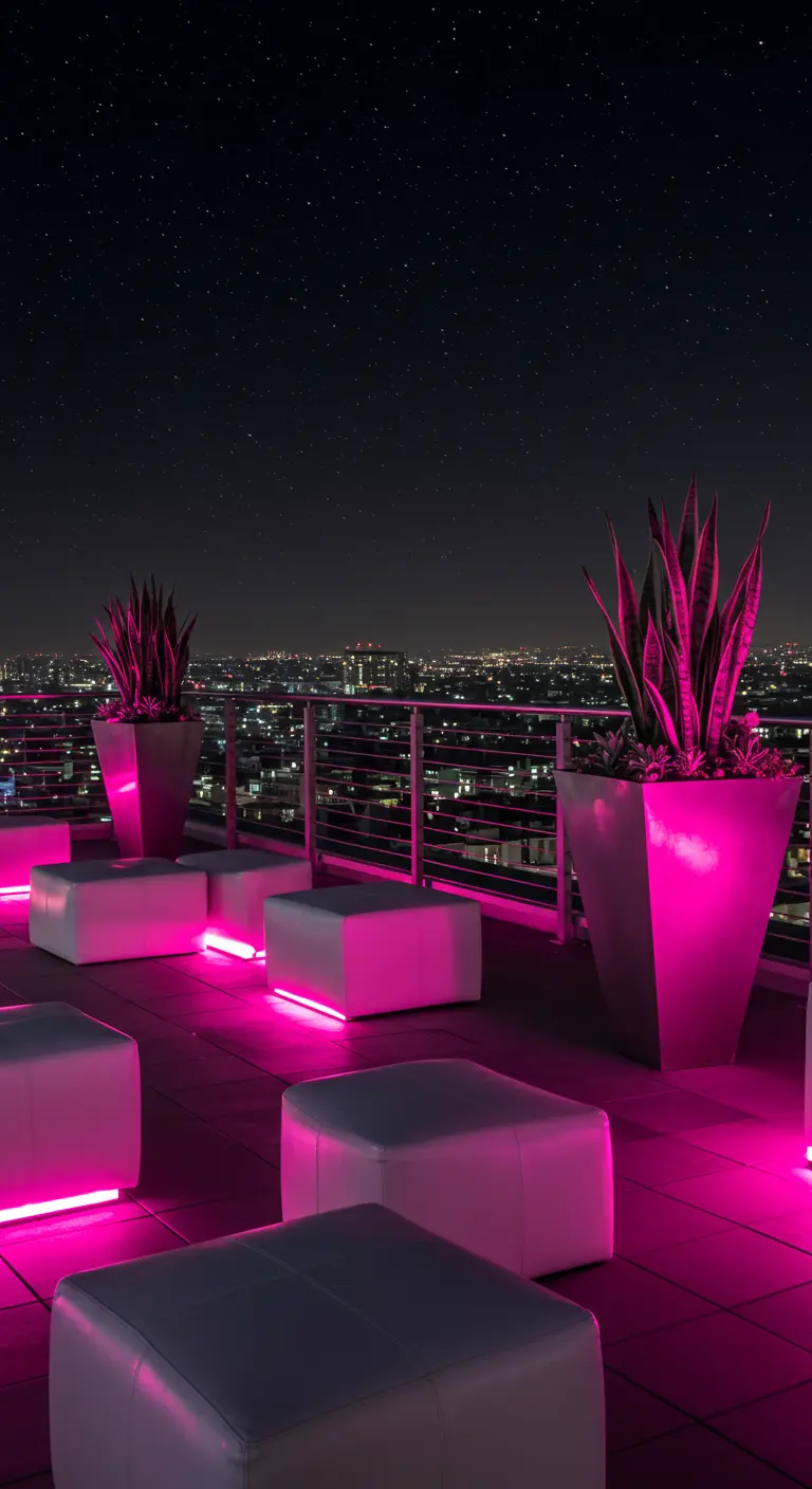 Rooftop lounge with bright pink LED lighting, white poufs, and silver planters with succulents.