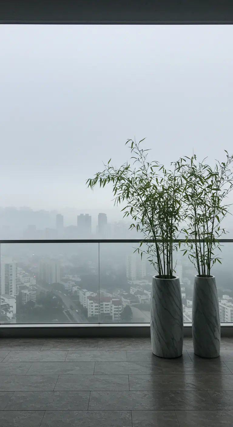 Two tall marble planters with bamboo on a balcony overlooking a foggy city.