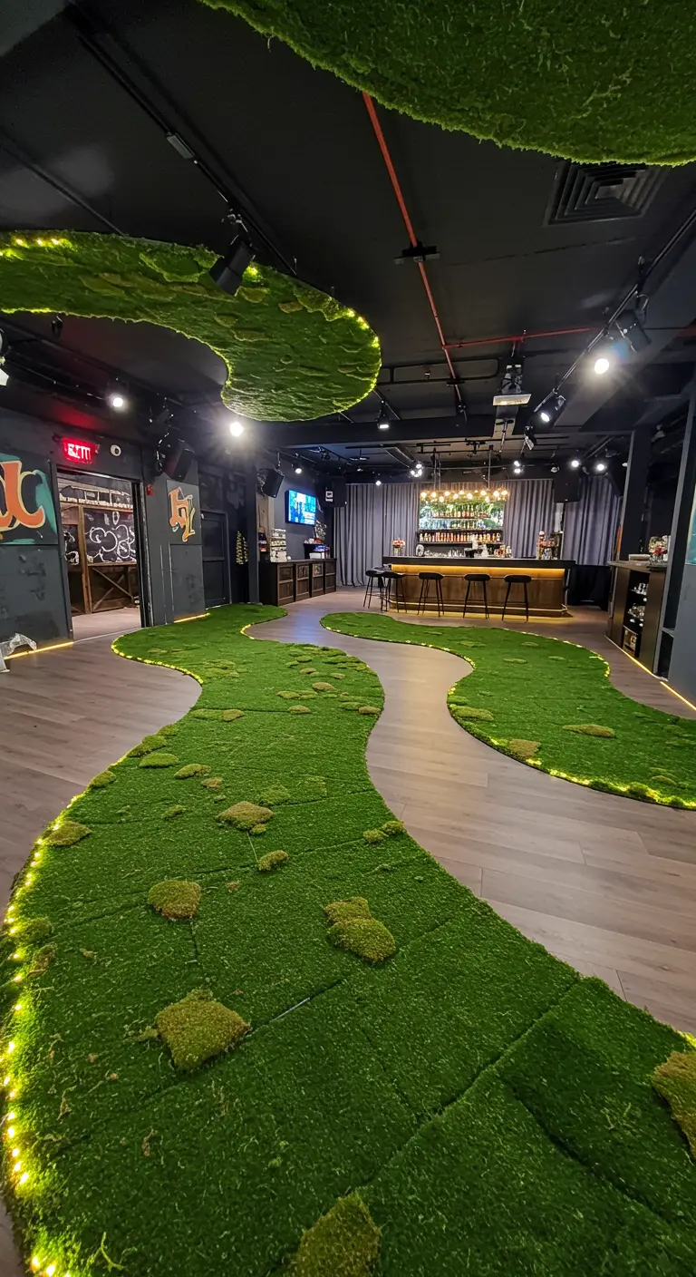 A winding indoor path made of artificial turf and moss, lined with lights.