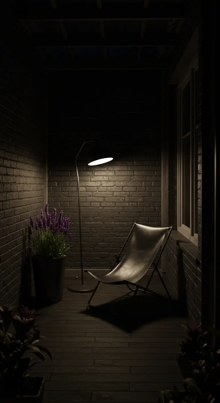 A dark patio at night with a single lamp illuminating a modern chair and a pot of lavender.