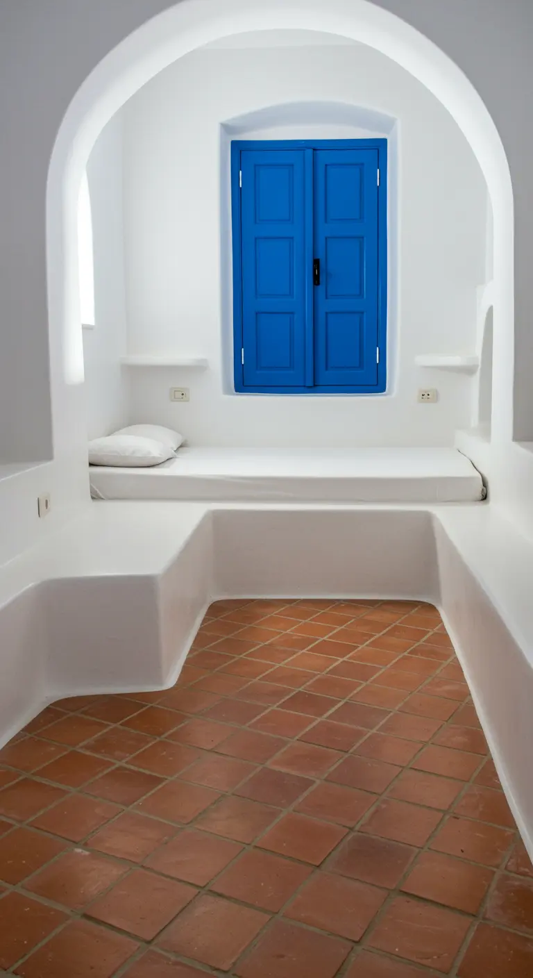 Whitewashed bedroom nook with a bright blue window and terracotta tile floor.