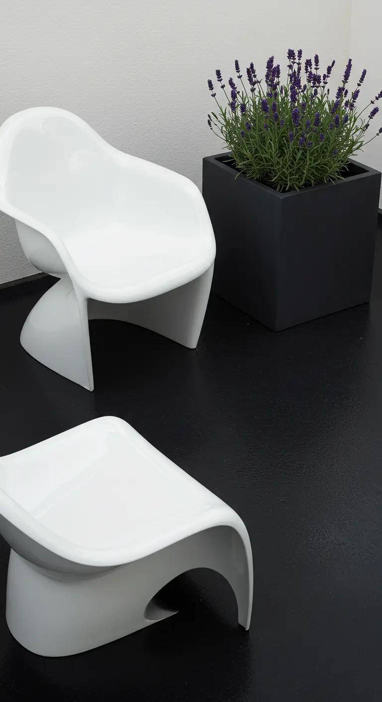 Two sculptural white chairs and a black planter on a glossy black patio floor against a white wall.