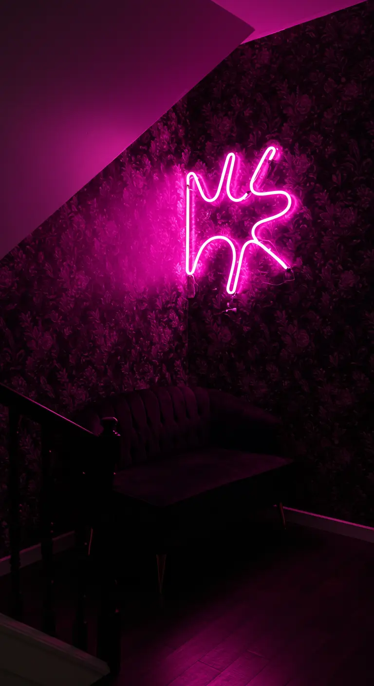 A dark lounge nook under the stairs with a pink neon sign and a black settee.