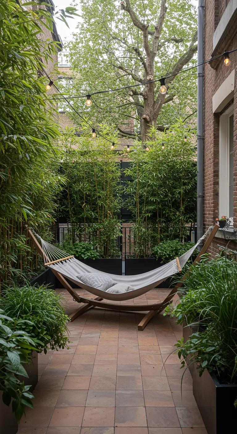 A brick-paved patio enclosed by tall bamboo in modern planters, with a freestanding hammock in the center.