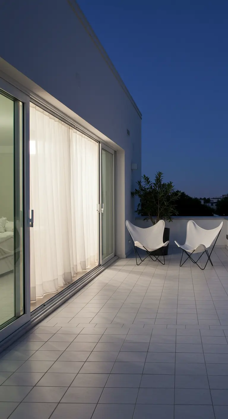 A seamless transition from a bedroom to a white tiled terrace with two butterfly chairs.