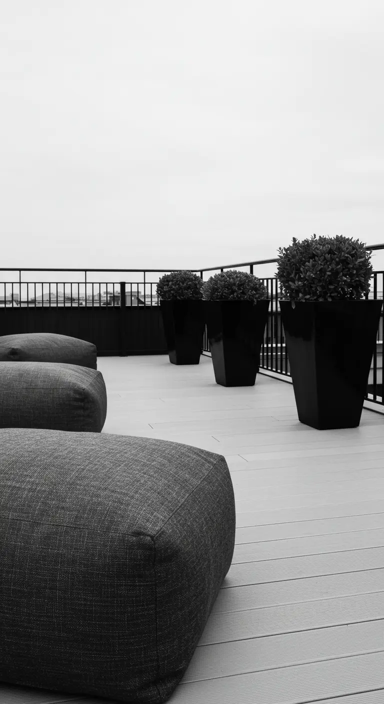 A monochrome rooftop with grey textured poufs and glossy black planters against a black railing.