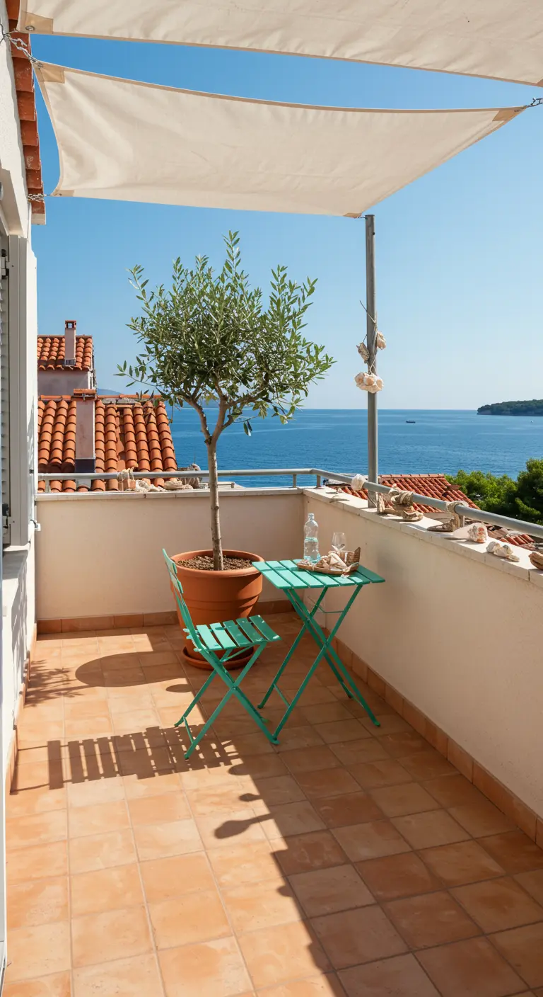 A balcony with an olive tree and a turquoise bistro set under a white sailcloth sun shade.